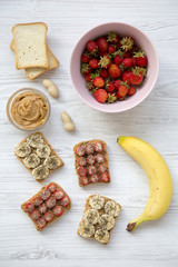 Healthy breakfast with ingredients, diet concept. Vegan toasts with peanut butter, fruits and seeds over white wooden background, flat lay.