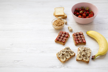 Healthy breakfast with ingredients, diet concept. Vegan toasts with fruits, seeds, peanut butter over white wooden surface, selective focus. Copy space.