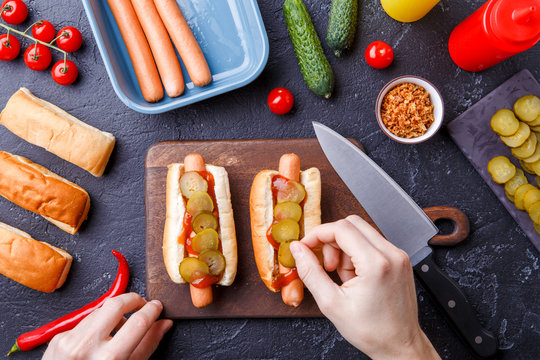 Photo on top of two hotdogs on cutting board on table with human hands