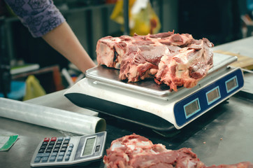 The seller of meat weighs fresh beef meat on scales.