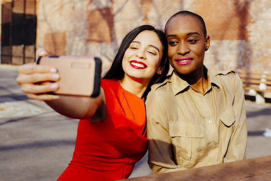 Portrait two friends taking selfie while sitting at a table in an urban park