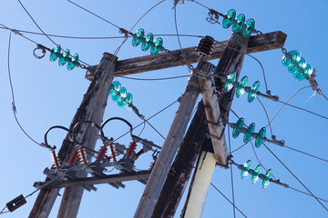 A wooden electric pole with many cables and insulators against clear blue sky