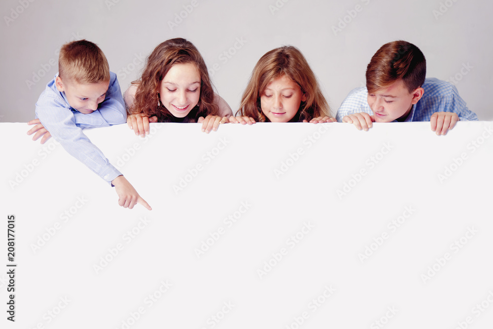 Wall mural Children looking down behind white empty banner. Little kid behind pointing to white wall.