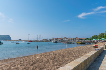 Fototapeta premium CZARNOGÓRA, BUDVA - CZERWIEC 05/2017: Odważni turyści kąpią się w chłodnej wodzie na plaży w pobliżu przystani jachtowej.
