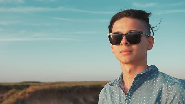 Portrait of a cheerful young man in sunglasses with a crew haircut smiling and getting pleasure from the view of the Black Sea on a sunny day in summer