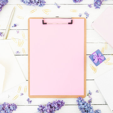 Minimalistic composition with clipboard, envelope, pen, lilac flowers and box on white background. Flat lay, top view. Freelancer or blogger concept.