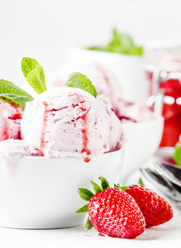 Strawberry ice cream with jam topping, decorated with green mint leaves, gray background, selective focus