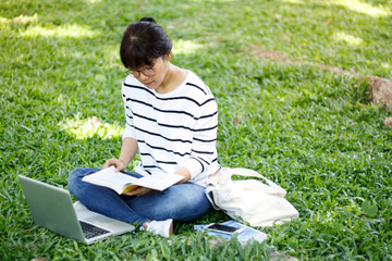 Naklejka na ściany i meble A portrait of an Asian college student on campus. Asian female student reading a book with diligence while sitting in the university. Copy space.