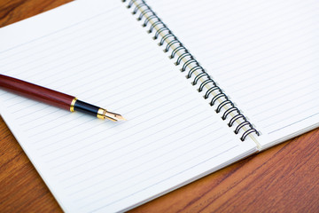 Naklejka premium Fountain pen or ink pen with notebook paper on wooden working table with copy space, office desk concept.