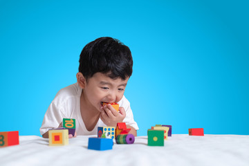 3 years old little cute Asian boy play toy or square block puzzle at home on the bed, kid lying learn by playing block shape or pieces, education and healthy concept idea.