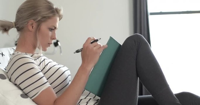 Young woman studying, reading, writing, drawing, relaxing on bed in apartment or dorm