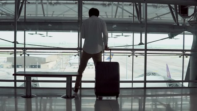 4K. Male Young passenger using smartphone walking with suitcase luggage and sitting on bench in departure area of airport terminal. Asian businessman on business trip. Modern travel lifestyle concepts