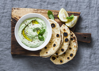 Avocado goddess sauce with whole grain flatbreads on a rustic cutting board on a grey background,...