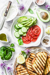 Ingredients for sandwiches - cream cheese, grilled bread, avocado, tomatoes, cucumbers, chives on a light background, top view. Summer picnic food concept. Flat lay