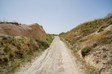 Fototapeta na wymiar Walking unpaved rough sand trail route through landscape of dried ancient red valley with clear sky background, Cappadocia