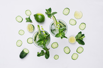 Ingredients for cooking cold spring drink with cucumber, pieces of lime, fresh leaves mint and ice cubes on soft white background, top view.