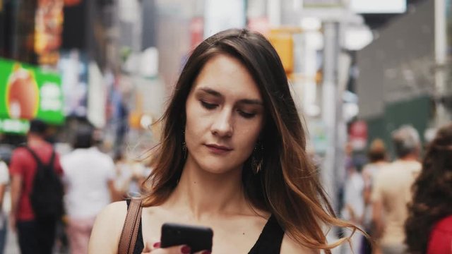 Portrait of young beautiful woman using smartphone if crowded downtown of New York, America. Girl type message.