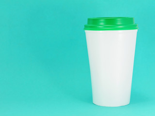 white plastic coffee cup with green lid on a blue background, front view with copy space