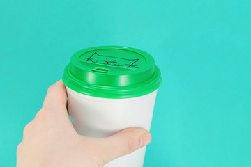 white plastic coffee cup with green lid in hand on a blue background, view from above with copy space
