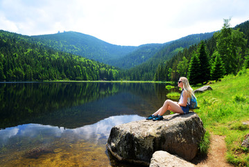 Fototapeta na wymiar Tourist sitting on stone by moraine lake Kleiner Arbersee in National park Bavarian forest. Germany.