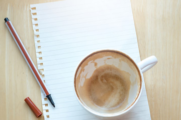 Top viwe of modern workplace with office supplies, notebook with felt-tip pen, Roasted coffee beans and Cappuccino coffee cup on wooden table.  Flat lay design and copy space concept.