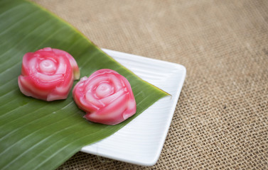Sweet pink flower shape Thai layer cake on fresh green banana leaf over blurred hessian texture background