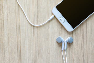 White earphones with smartphone on office wooden desk background