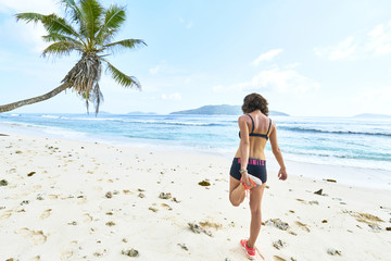 young woman stretching before the workout on tropical beach, seychelles, digue island