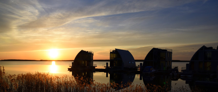 Abendidylle mit Sonnenuntergang am Geierswalder See mit Silhouetten von vier  schwimmenden H&auml;usern