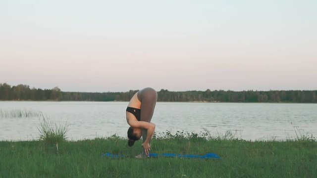 Woman doing yoga in quiet scenery. Beautiful young girl wearing sports clothes doing yoga in morning at lake, sun salutation on blue yoga mat. Yoga, sport and healthy lifestyle concept with copyspace