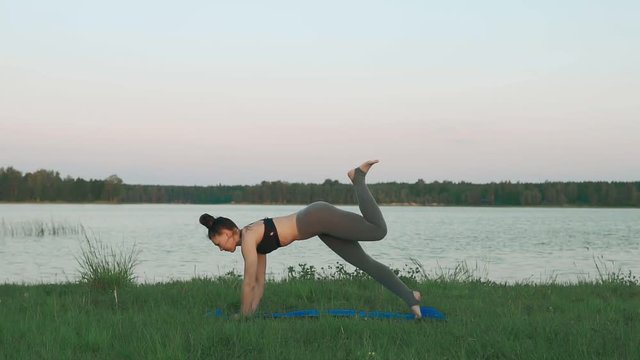 Woman doing yoga in quiet scenery. Beautiful young girl wearing sports clothes doing yoga in morning at lake, sun salutation on blue yoga mat. Yoga, sport and healthy lifestyle concept with copyspace