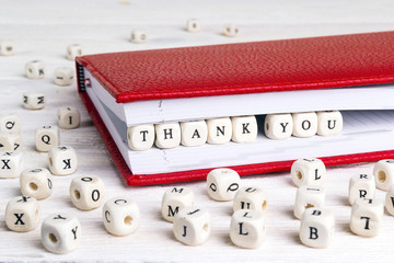 Word Thank you written in wooden blocks in red notebook on white wooden table.