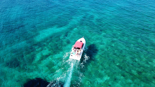 Aerial drone bird's eye view photo of small boat cruising in tropical emerald clear waters