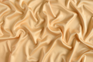 Close up of ripples in gold colored silk fabric. Satin textile background.