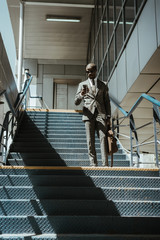 Obraz na płótnie Canvas Young african american businessman using smartphone while walking on stairs