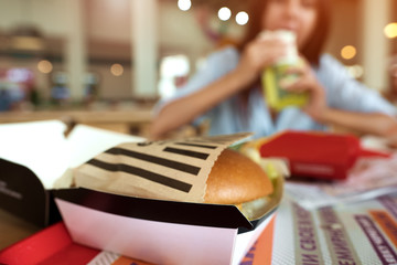 Blurred image of young woman eating fresh hamburger indoors. Fastfood concept