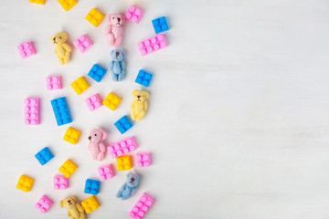 Top view on multicolor toy bricks and plush bears on white wooden background.