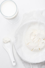 top view of cottage cheese on cheesecloth glass of milk with spoon on white surface