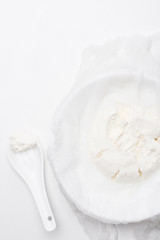 top view of cottage cheese on cheesecloth with spoon on white surface