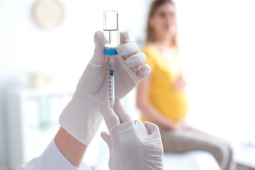 Doctor holding ampule with vaccine and syringe for patient in clinic, closeup