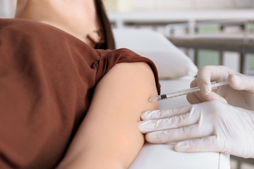Doctor vaccinating female patient in clinic, closeup