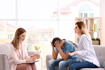 Young female psychologist working with teenage boy and his mother in office