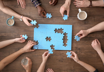 People with puzzle on wooden background, closeup of hands. Unity concept