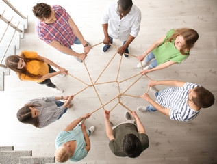 People holding rope together indoors, top view. Unity concept