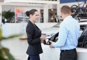 Young saleswoman working with client in car dealership