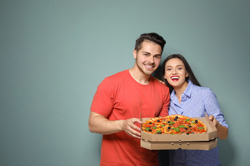 Attractive young couple with delicious pizza on color background