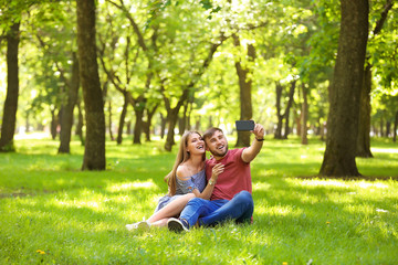 Fototapeta premium Happy young couple taking selfie on green grass in park
