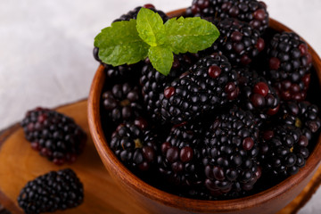 Ripe organic blackberries in wooden bown on gray stone background