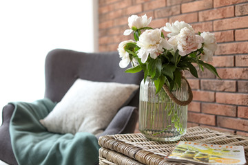 Vase with beautiful flowers on wicker trunk indoors. Interior decor element