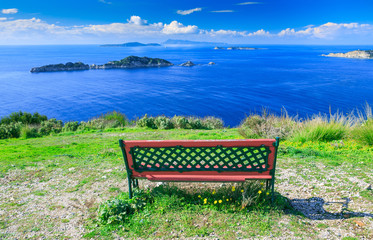 Naklejka na ściany i meble Awesome view from red wooden bench to the coastline sea bay with crystal clear azure water, distant islands in the calm warm sea. Beautiful summer seascape. Agios Stefanos cape. Afionas. Corfu. Greece